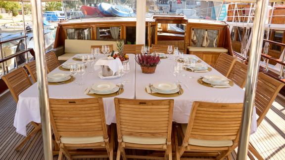 Beautifully set dining table on the deck of the gulet Linda, surrounded by wooden chairs.